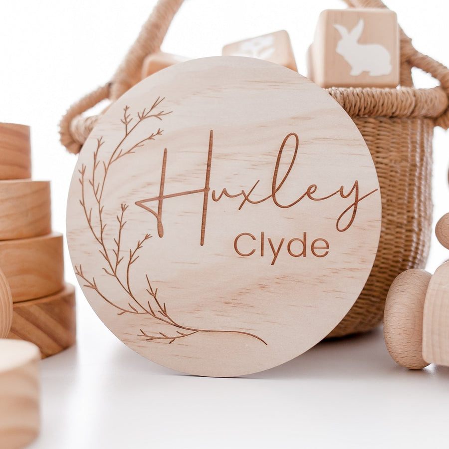 Hello Fern wooden whimsical name plaque featuring baby's name custom-etched on wooden disc with natural wooden toys surrounding.