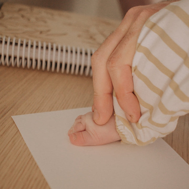 Dad pressing child's foot down to make foot print on inkless print kit paper.