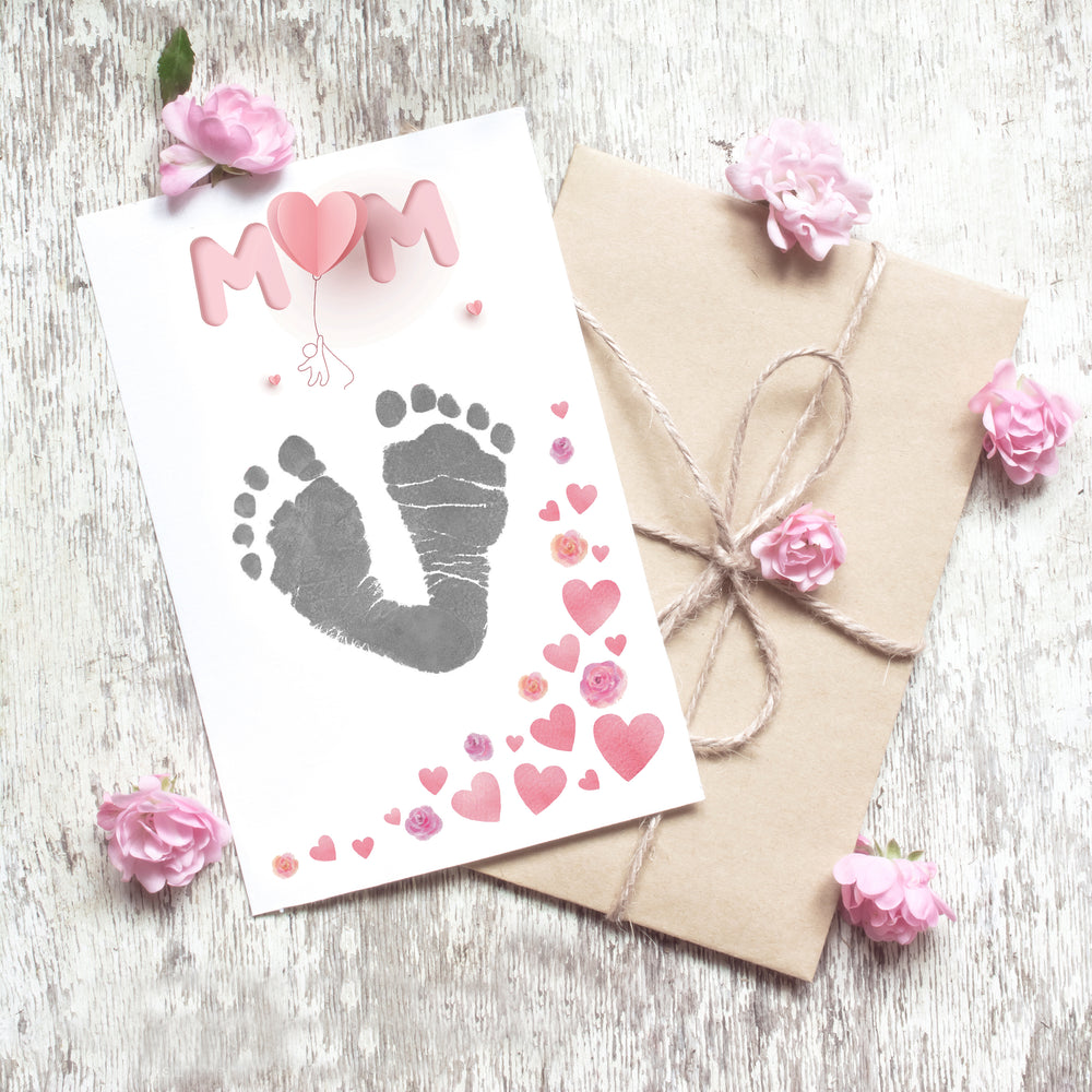Closeup of "MUM" print sheet from Mother's Day inkless print kit showing baby's footprints in grey.