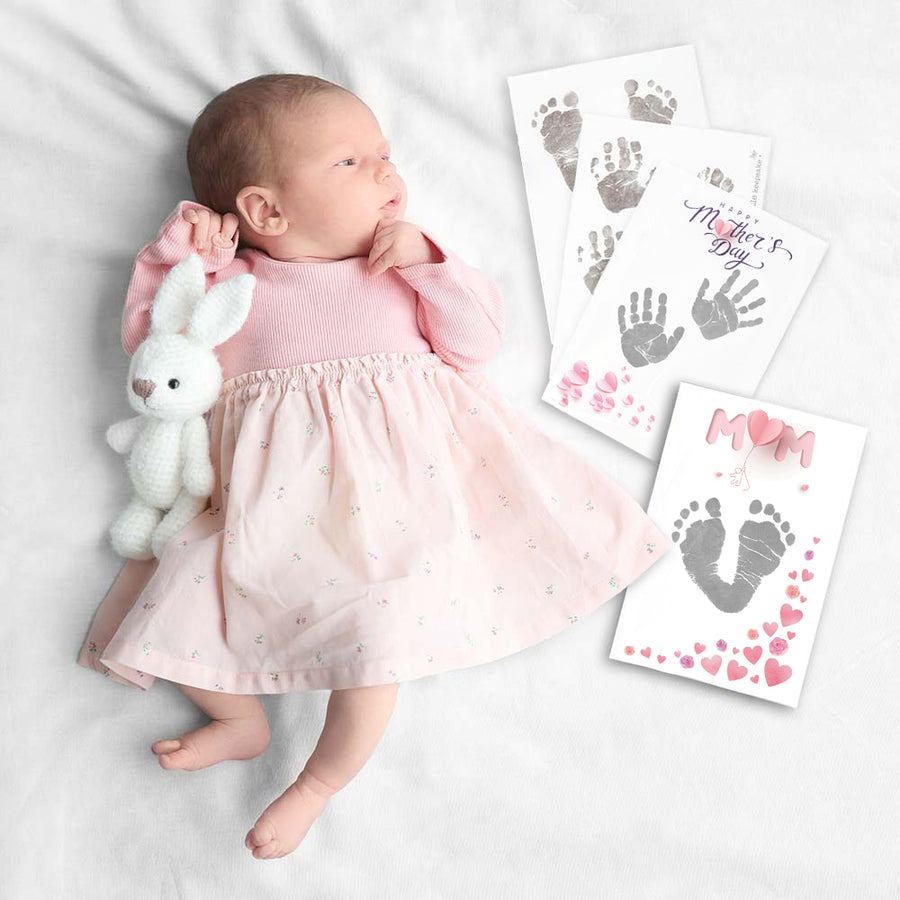 Baby girl flatlay with mothers day inkless print kits showing baby's footprints and handprints.