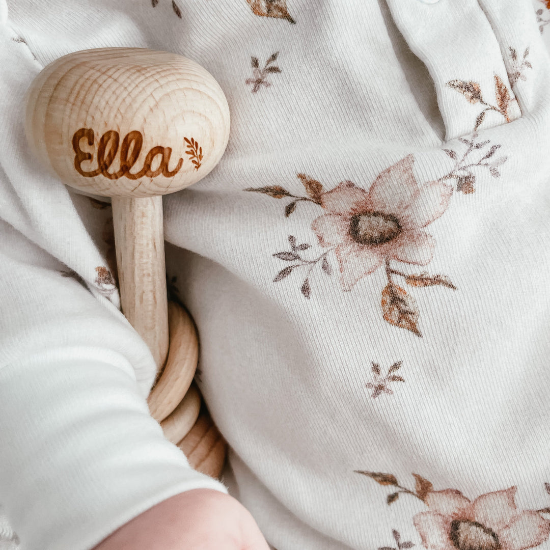 Custom wooden baby rattle with name Ella etched in to rattle tucked under baby's arm.