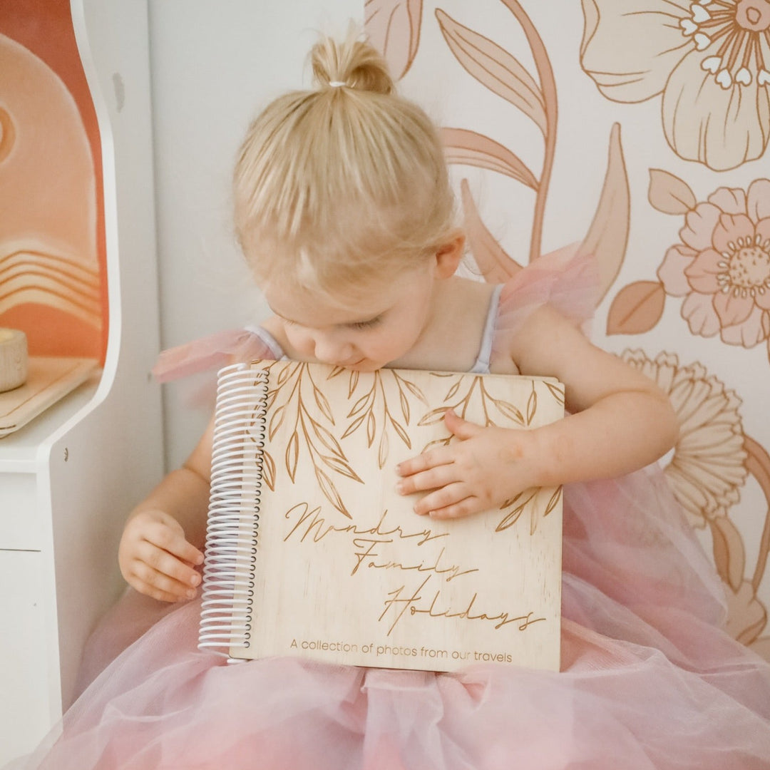 Little girl in tutu holding a Hello Fern wooden photo album for her family's holidays.
